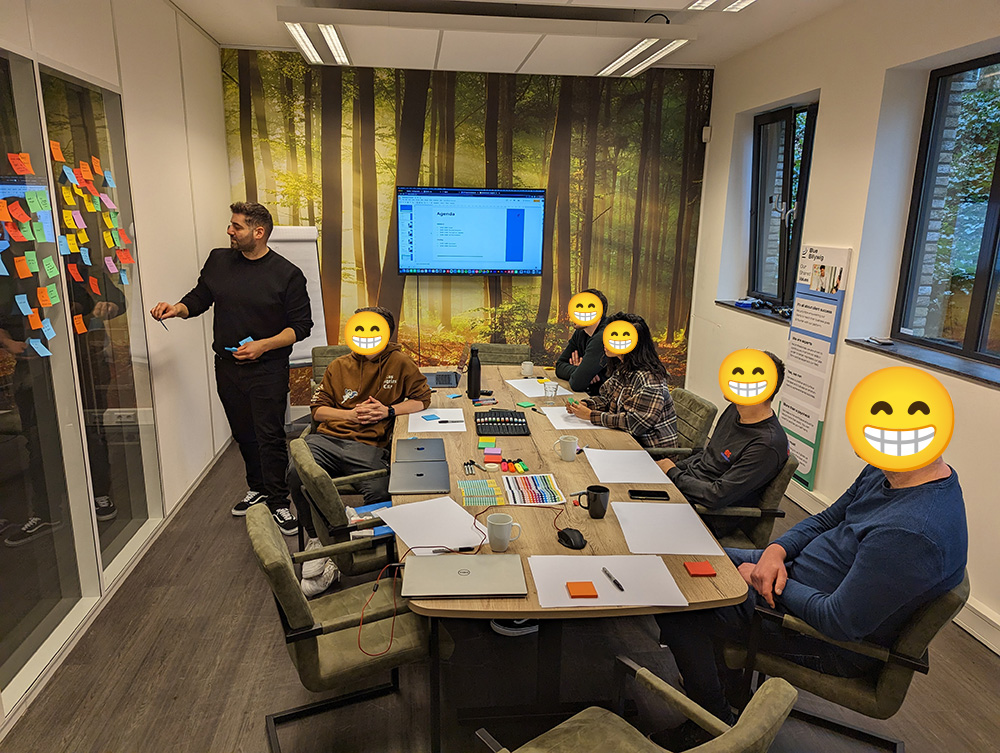 A brainstorm session in a meeting room with colleagues around a table and sticky notes on a glass wall.