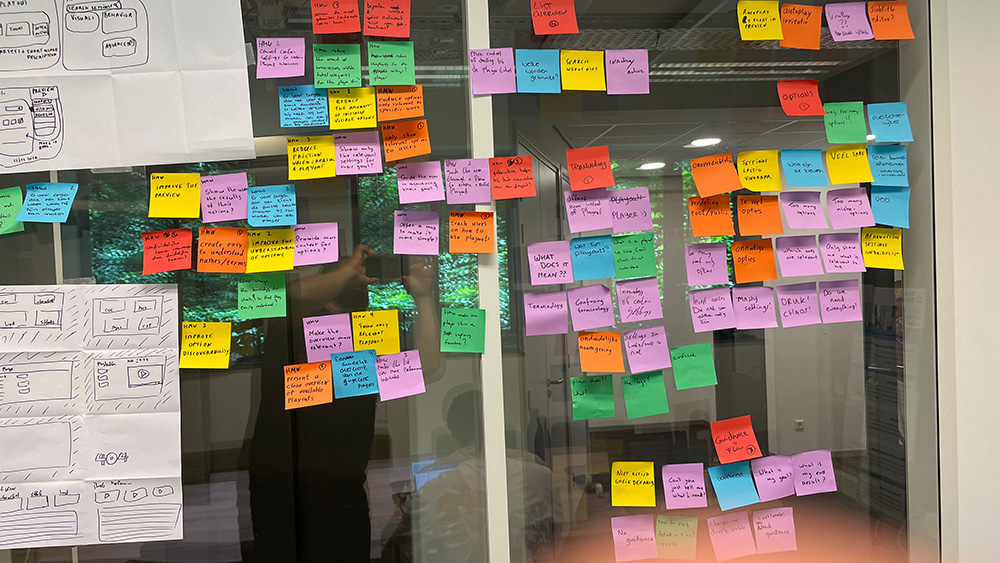 Close-up of sticky notes with how-might-we questions next to paper sketches.